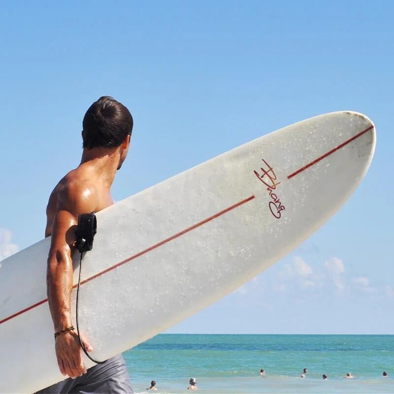 Surfer carrying a Bhang-branded longboard toward the ocean