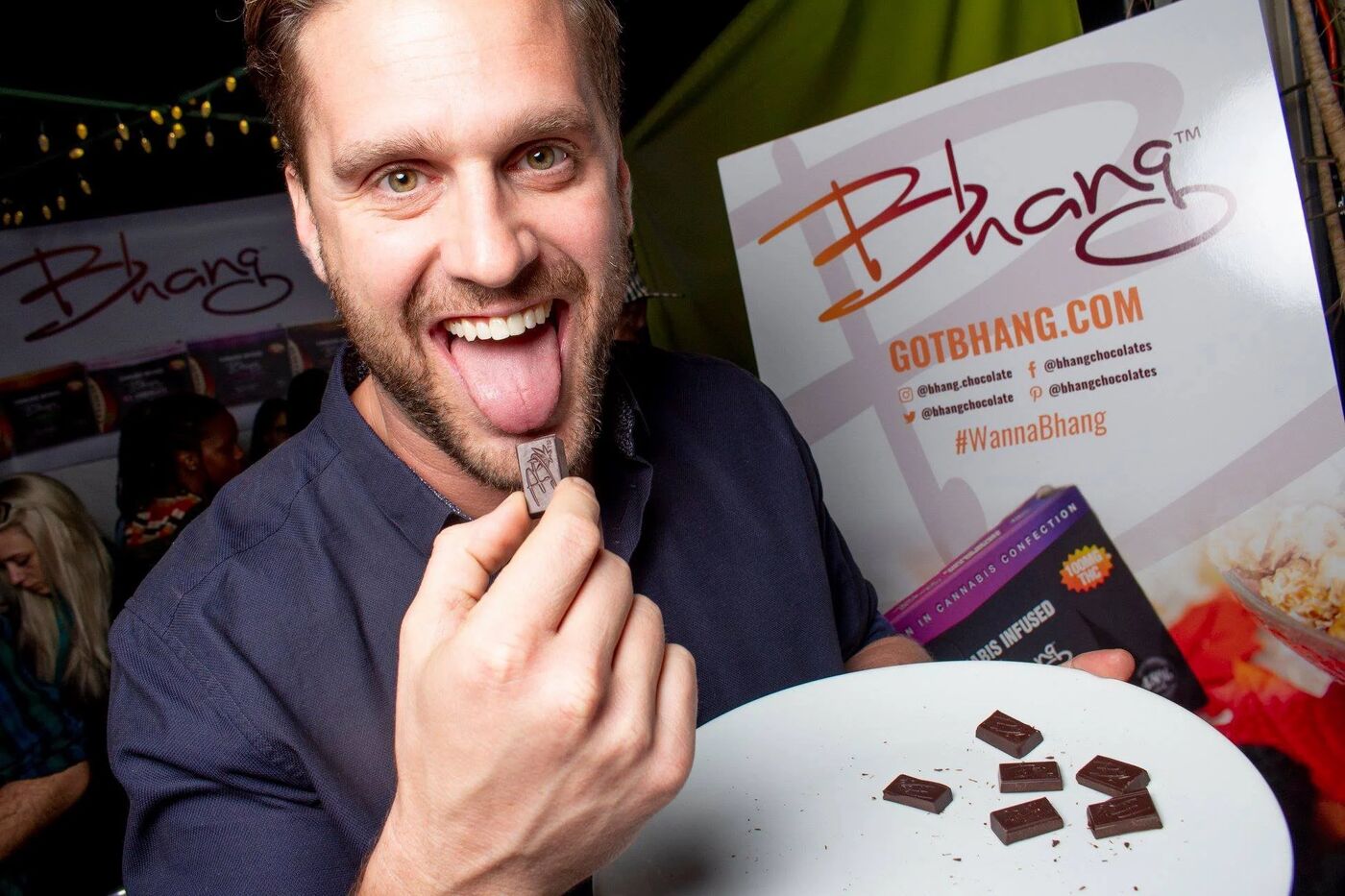 Smiling guest eating a piece of Bhang chocolate in front of a Bhang banner