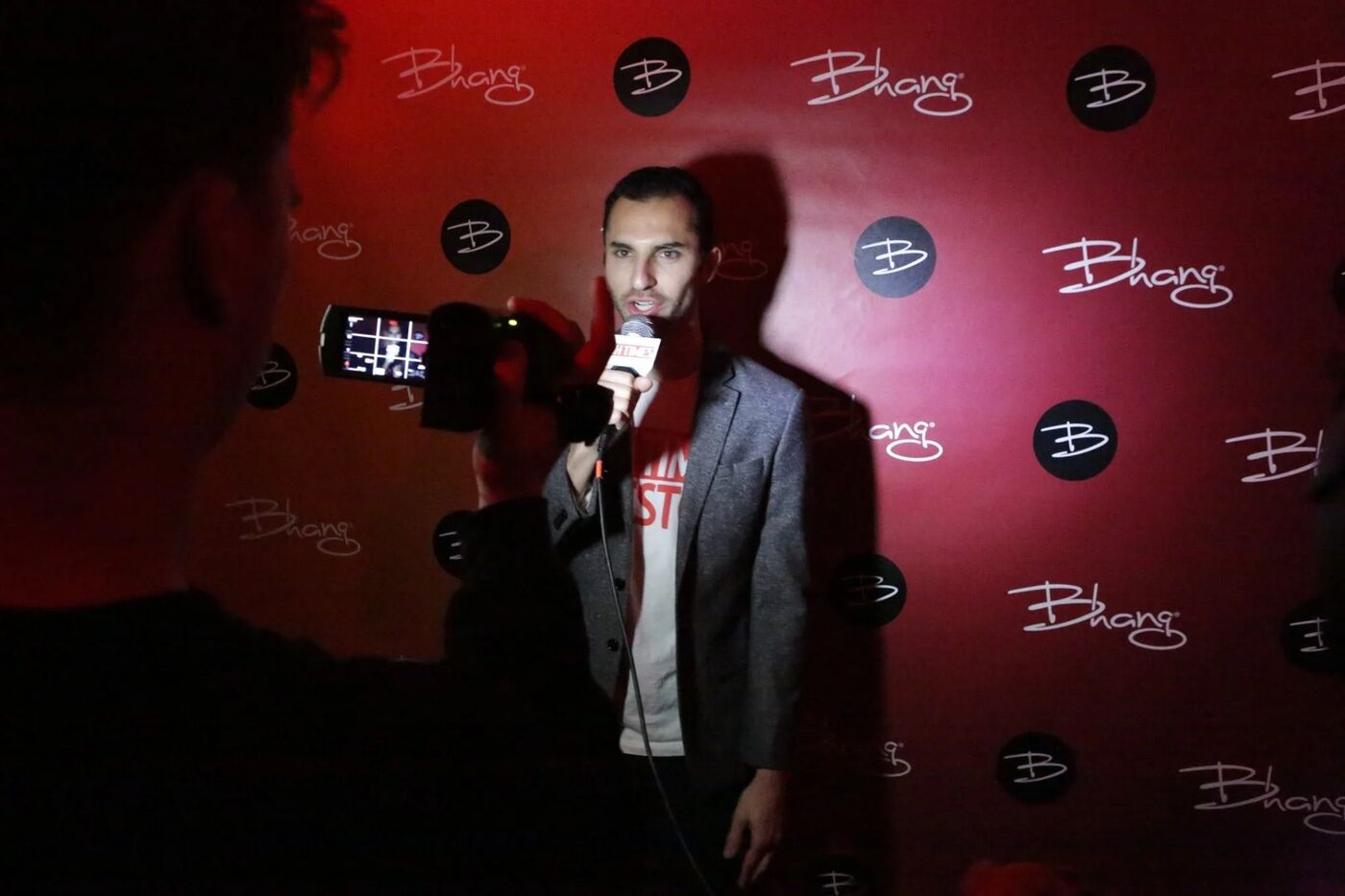 Host speaking into a microphone on camera in front of the Bhang backdrop