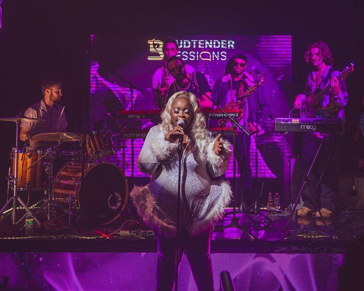 Singer performing in a white fur coat with a band at Budtender Sessions