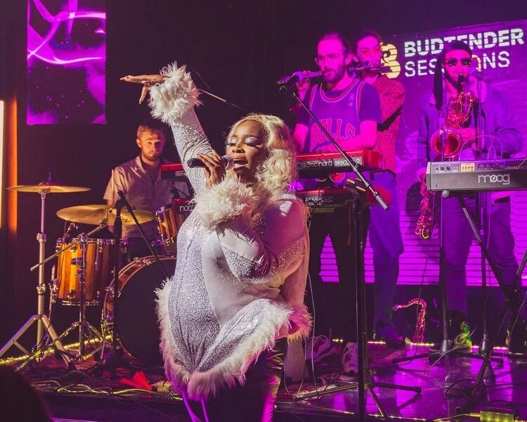 Singer and band performing under purple light at Budtender Sessions