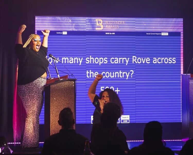 Budtender Sessions game show host on stage with a trivia question about Rove on screen
