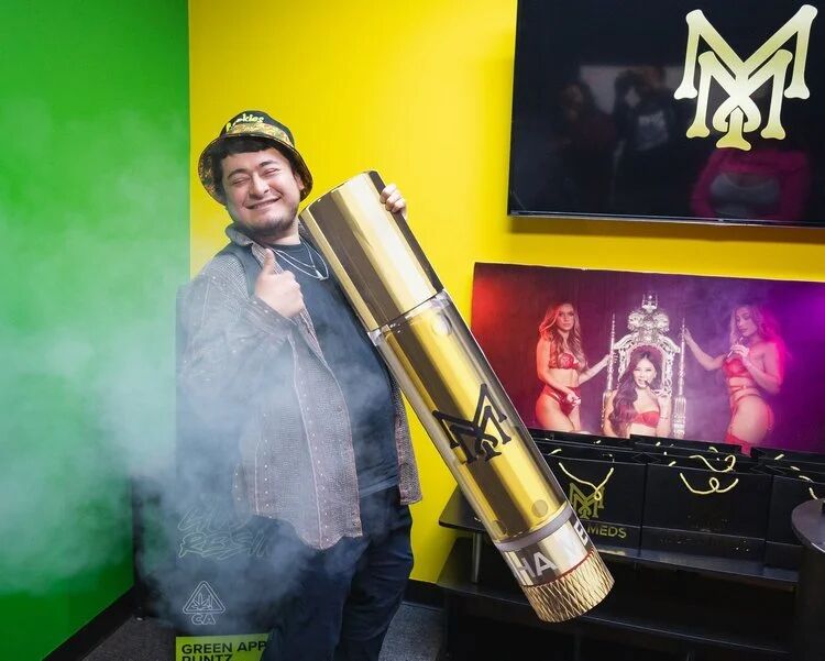Guest posing with an oversized gold joint display at a Budtender Sessions event