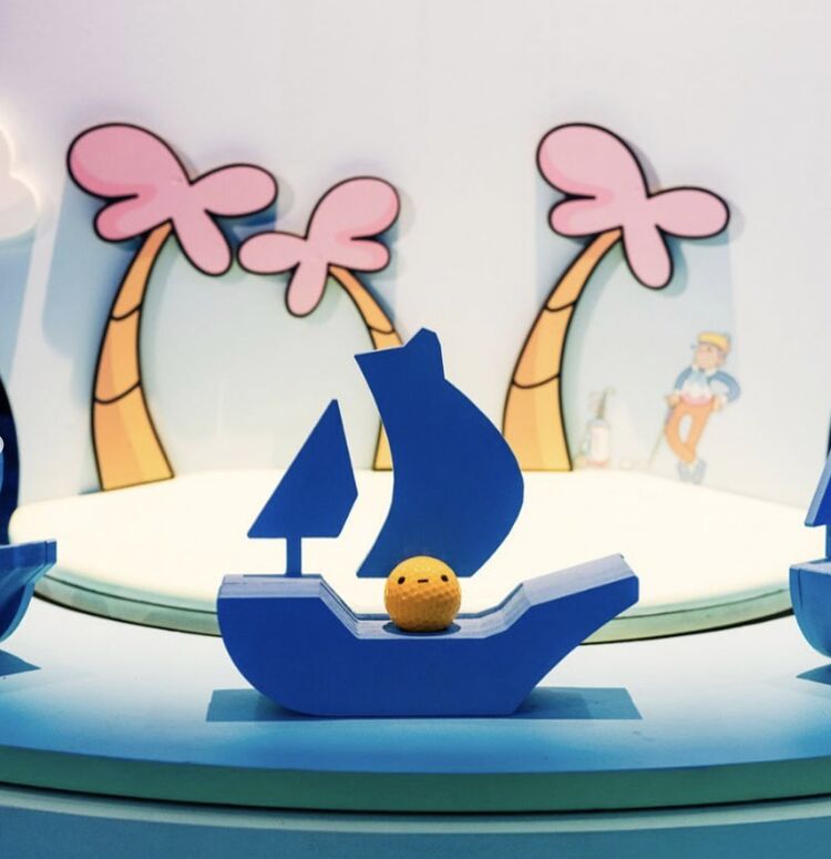 Mini-golf hole with a blue OpenSea sailboat and cartoon palm trees