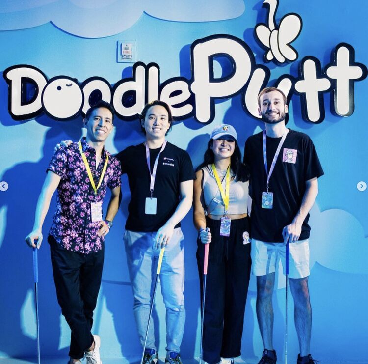 Four friends holding putters in front of the DoodlePutt sign