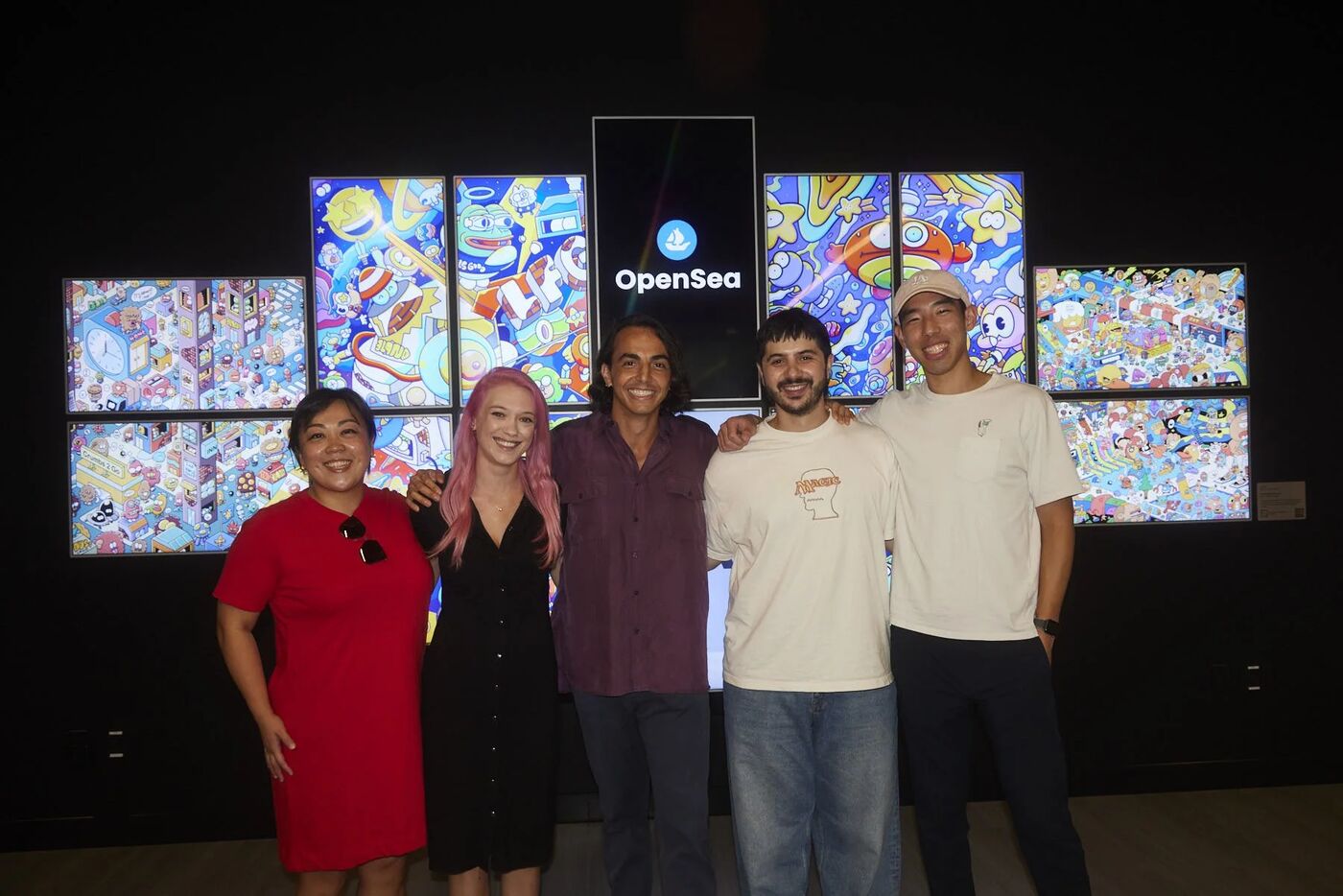 Friends of OpenSea hosts posing in front of a wall of colorful digital art screens