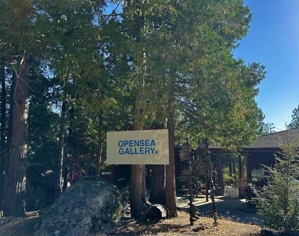 OpenSea Gallery sign among the pine trees at FWB Fest