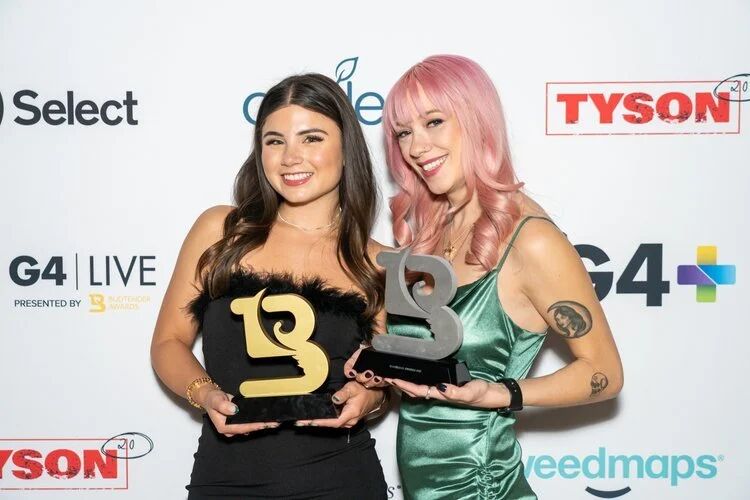 Two winners holding Budtender Awards trophies at the G4 Live step-and-repeat