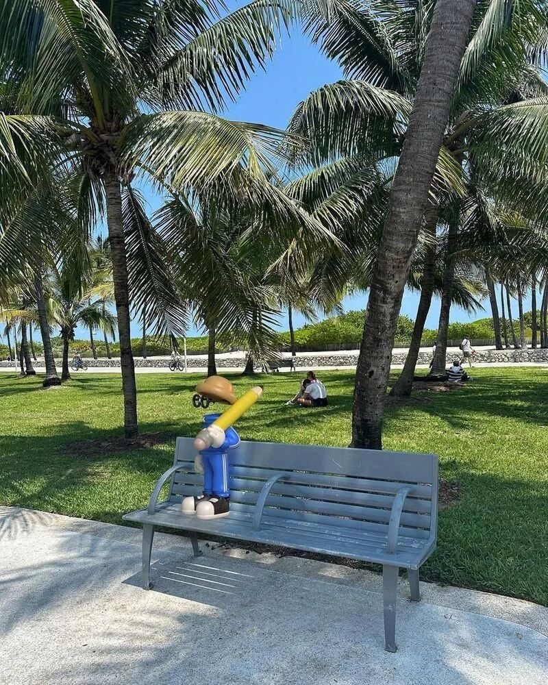 Invisible Friends toy sitting on a park bench under palm trees in Miami