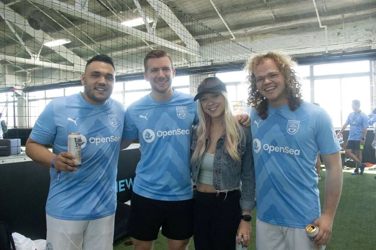 Four people in OpenSea soccer jerseys at an indoor field