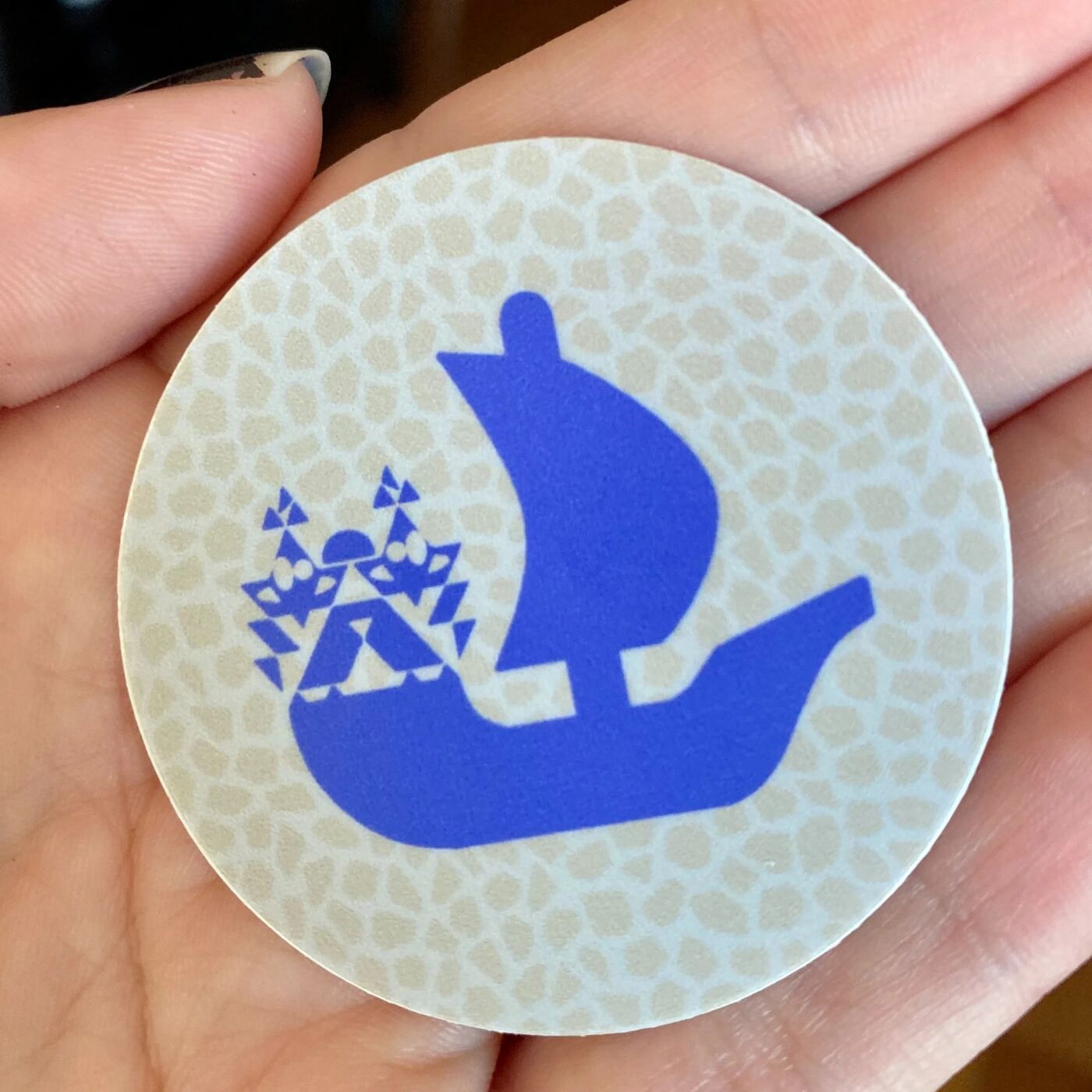 Hand holding a round OpenSea sailboat sticker
