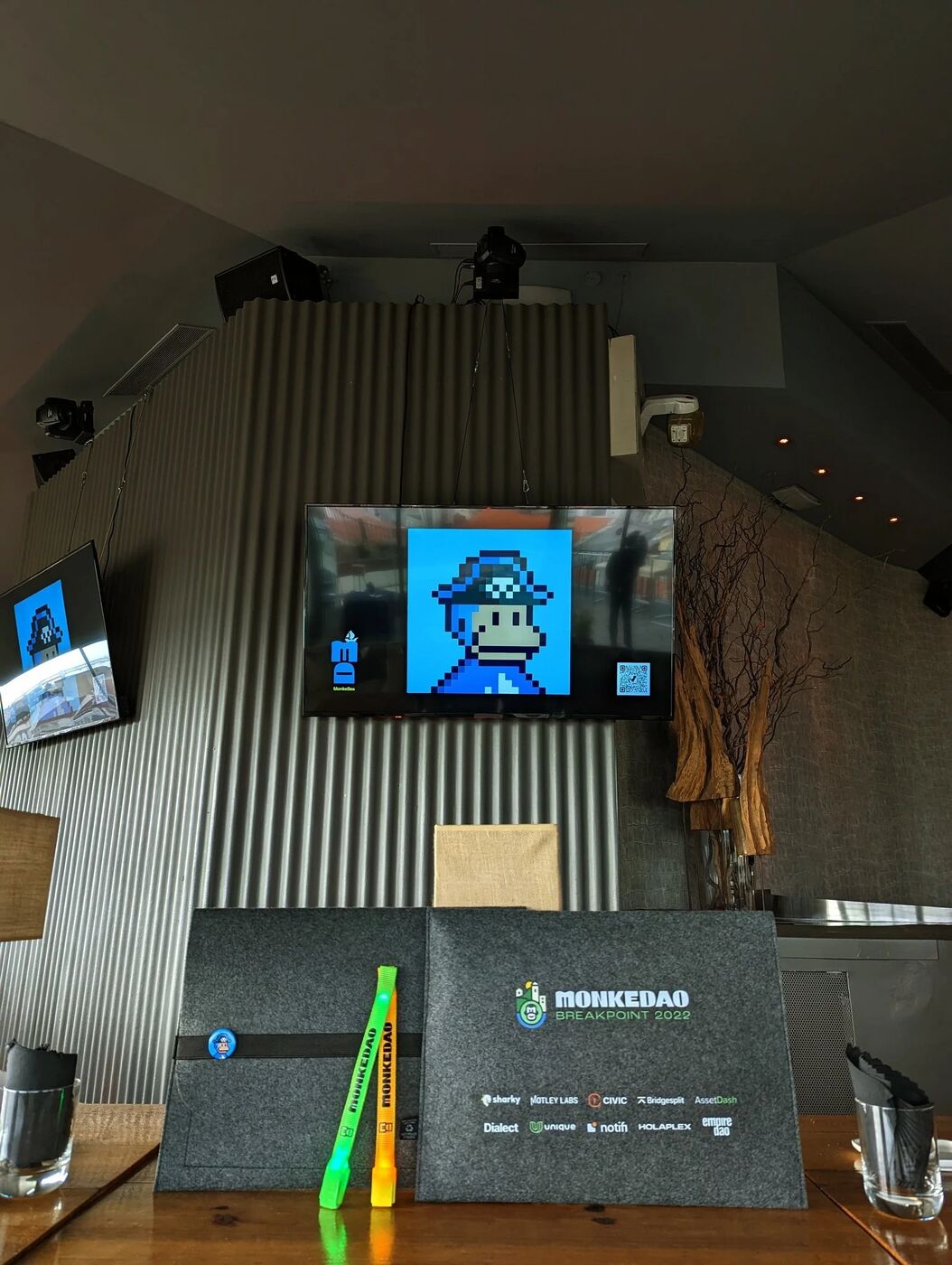MonkeDAO event space with pixel-art monkey on screen and branded table signage