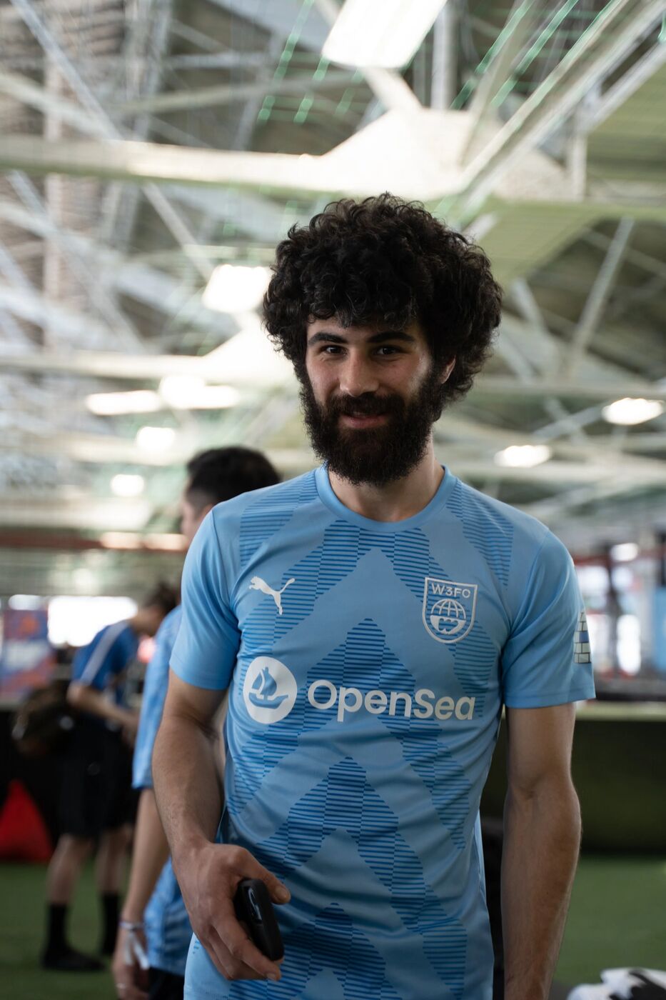 Player in an OpenSea jersey smiling on the sideline